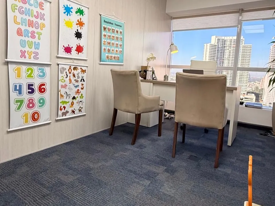 Sala de atendimento do consultório, com cartazes de alfabeto, números e fonemas na parede